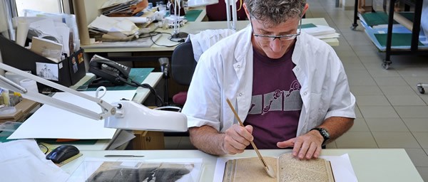 Yuval Sitton, a paper conservator at Yad Vashem, is dry-cleaning a Holocaust-era diary in the paper conservation lab. Photo Yad Vashem