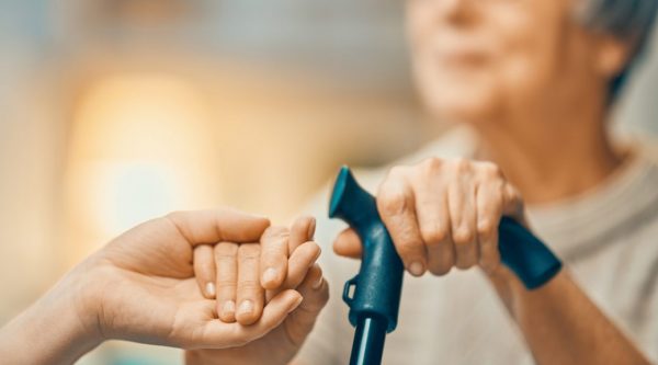 Person holding the hand of a person who uses a walking cane