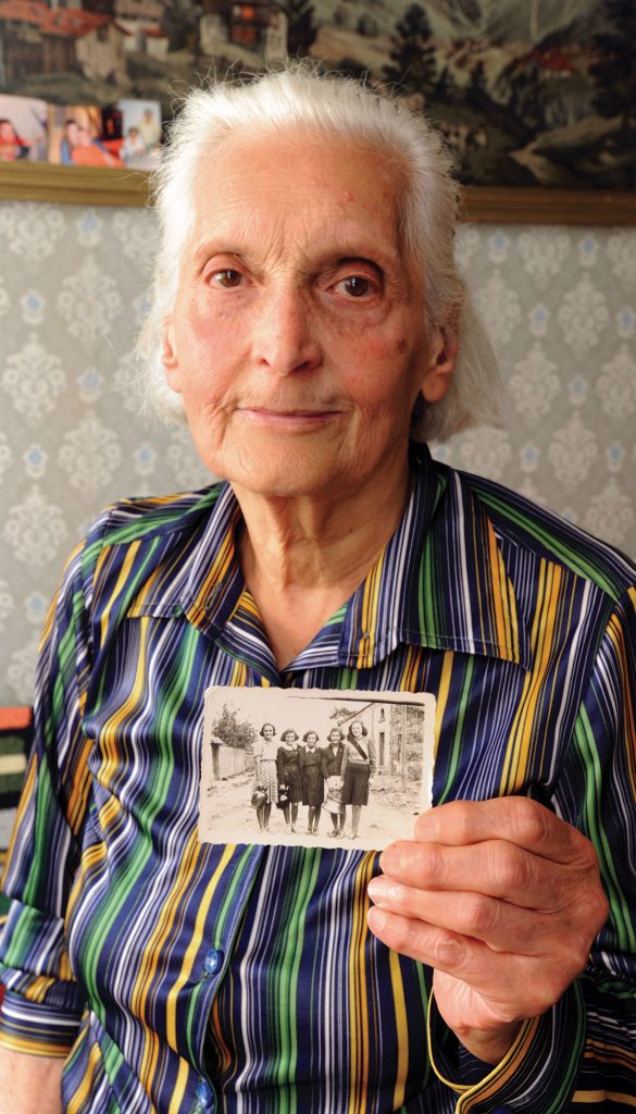 Survivor poses for photo and holds up historical photograph of her family